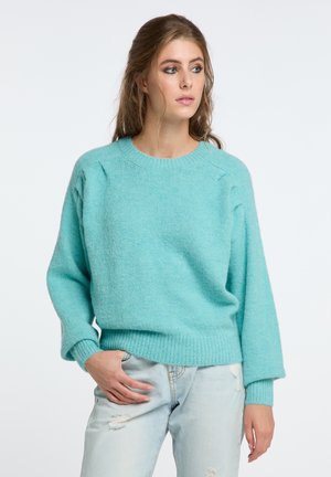 Licht turquoise trui gemaakt van zacht materiaal, met een ronde halslijn, raglanmouwen en een geribde zoom, gecombineerd met lichte spijkerbroek.
