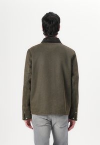 Olive-green jacket with a corduroy collar, snap-button cuffs, and a relaxed fit. Textured fabric and contrasting stitching detail.