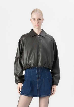 Veste bomber en simili cuir vert foncé avec une fermeture éclair, silhouette oversize et large col, associée à une jupe en denim.