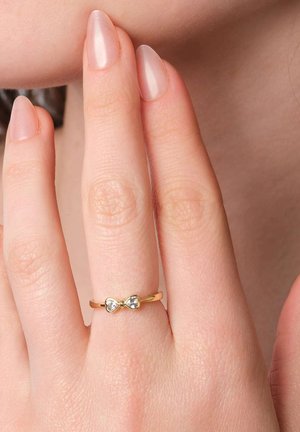 Gold ring featuring a bow design, set with two clear stones. The band has a smooth finish and is worn on a slender finger.