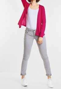 Fuksianvärinen neuletakki valkoisen toppin päällä, yhdistetty vaaleanharmaisiin skinny-farkkuihin ja valkoisiin tennareihin. Neuletakki on avoimella edustalla ja pehmeäkokoinen.