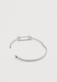 Brazalete de puño de metal plateado con un diseño elegante, que presenta dos acentos esféricos en tono dorado y un extremo abierto para facilitar su uso.