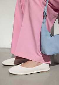 Bílé perforované slip-on boty s kulatou �špičkou a plochou podrážkou, doplněné růžovými širokými kalhotami a malou modrou kabelkou.