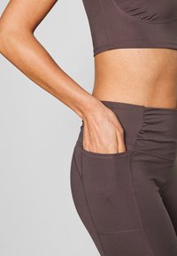 Brown athletic crop top and high-waisted leggings feature a side pocket and textured stitching for a fitted look.