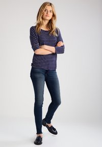 Top de rayas azul marino y blanco de manga larga, combinado con jeans ajustados oscuros de mezclilla y zapatos negros. Ajuste casual con un diseño relajado.