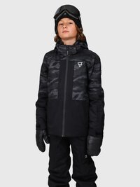Junge in schwarzer und grauer Camouflage-Ski-Jacke, schwarzen Schneehosen, schwarzen Handschuhen, Mütze und Skibrille auf dem Kopf, steht vor einem einfarbigen Hintergrund.