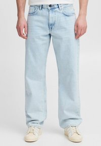Lichtblauwe denim jeans met rechte pijpen, vijf zakken, subtiele vervaging en een knoopsluiting. Gecombineerd met witte sneakers.