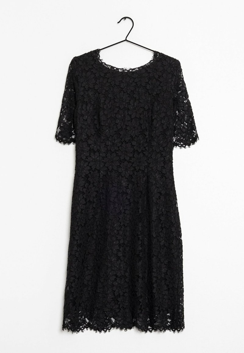 Robe en dentelle noire longueur genou avec manches courtes suspendue à un cintre noir sur fond blanc.
