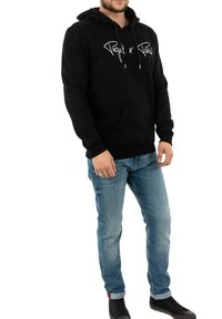 Zwarte hoodie met een buidelzak en trekkoord. Voorzien van een wit "Project x Paris" logo. Gedragen met lichte blauwe jeans en zwarte schoenen.