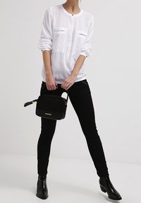 Vit långärmad blus med två framfickor, i kombination med svarta skinny jeans och en liten svart texturerad handväska. Svarta ankelstövlar fulländar looken.