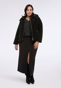 Černá prošívaná péřová bunda s kapucí, zlatým zipem a bočními kapsami, zkombinovaná s dlouhou černou sukní s rozparkem nad stehnem a černými botami.