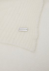 Écharpe tricotée blanche avec une texture côtelée, dotée d'une étiquette en argent rectangulaire portant l'inscription « REPEAT ». Fibres douces, couleur uniforme, sans motifs.