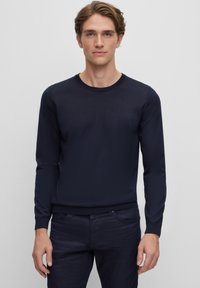 Pulover albastru închis, cu mâneci lungi și guler rotund, cu manșete din tricot. Textură moale, design simplu, asortat cu pantaloni negri.