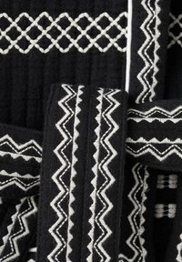 Svart textil med vita zigzag- och diamantmönster, med texturerad tyg och kontrasterande sömnadsdetaljer som framhäver designen.