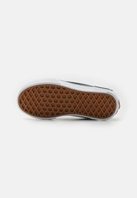Adidaș Vans cu o talpă din cauciuc albă, având un model texturat de prindere din brun. Partea superioară este compusă din secțiuni de pânză albă și neagră, cu accente roșii.