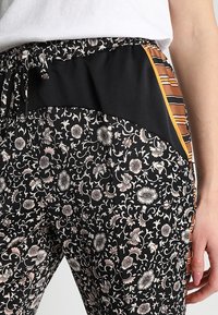 Bloemmotief broek met een zwarte basis, voorzien van een rekbare tailleband en zijkanten in zwart en gestreepte tinten oranje en bruin.