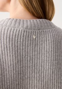 Gray ribbed sweater with a high neckline, featuring a small silver heart-shaped accent at the back. Soft, textured knit fabric.