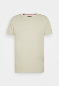 Light beige cotton T-shirt with a crew neck and short sleeves. Features a small, light-colored rectangular patch on the chest.