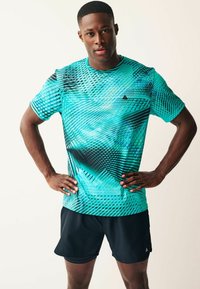 Sportisks īsām piedurknēm krekls tumši zilā krāsā ar dinamisku ģeometrisku rakstu, izgatavots no viegla auduma. Apvienots ar melniem sporta šortiem.