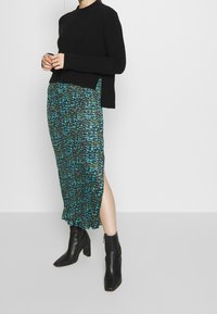 Svart stickad tröja kombinerad med en teal och svart mönstrad, plisserad midikjol med en sidoklyfta, kompletterad med svarta klackade ankelstövlar.