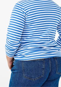 Blå och vit randig långärmad topp i ribbat tyg, i kombination med mörkblå denimjeans med bakfickor och en texturerad yta.