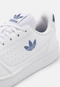 Weiße Ledersneaker mit blauen Akzenten, perforierten Seiten, einem Logo auf der Zunge und einer strukturierten Gummisohle.