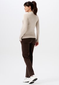 Beige langemouw top en bruine broek met zakken, aangesloten ontwerp, zachte textuur, gecombineerd met witte sneakers met grijze accenten.