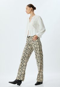 Blouse blanche texturée avec un bouton à l'avant et un ourlet froncé ; associée à un pantalon ajusté imprimé serpent en crème et noir ; bottes à talons noires.