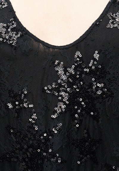 Črno čipkasto oblačilo z okraski v obliki zvezdastih bleščic. Tkanina je lahka s prosojno teksturo. V-izrez.