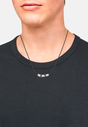 Silberfarbene Bar-Halskette an einem schwarzen Band, ausgestattet mit fünf metallischen rechteckigen Perlen, getragen über einem schwarzen T-Shirt mit Rundhalsausschnitt.