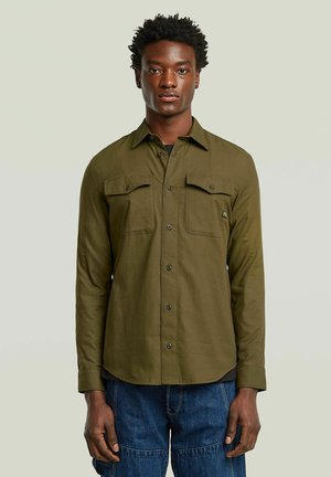Chemise à manches longues vert olive avec deux poches poitrine et boutons noirs. Présente un col pointu et une coupe droite à l'ourlet.