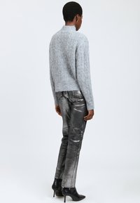 Grå striktrøje med høj hals, kombineret med skinnende metallic sølvbukser og sorte stiletter. Glatte teksturer og tætsiddende design.