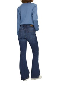 Blauwe lange mouw top met opgeblazen schouders, gecombineerd met donkerblauwe uitlopende jeans met twee achterzakken en een tan leren label.