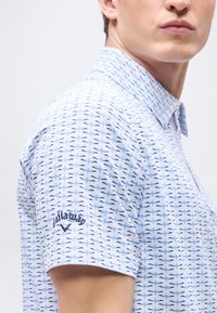 Ανδρικό μοντέλο που φοράει ανοιχτό μπλε πόλο μπλουζάκι γκολφ με σχέδιο και το λογότυπο Callaway κεντημένο στο αριστερό μανίκι.