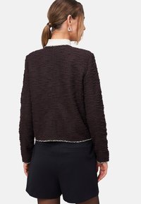 Gestructureerde donkerbruine cropped trui met een witte kraag en een zoom van zilverdraad, gecombineerd met zwarte shorts, wat een casual ontwerp benadrukt.
