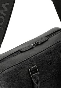 Black leather bag with a textured finish, featuring a zippered top, adjustable strap, and black hardware accents. Logo details present.
