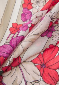 Tela con estampado floral que presenta flores rojas, rosas y beiges sobre un fondo claro; textura suave con pliegues suaves.