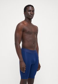 Férfi sötétkék sportshort, sima, rugalmas anyagból készült, széles derékpánttal és testhezálló kialakítással a kényelem és a támasz érdekében.