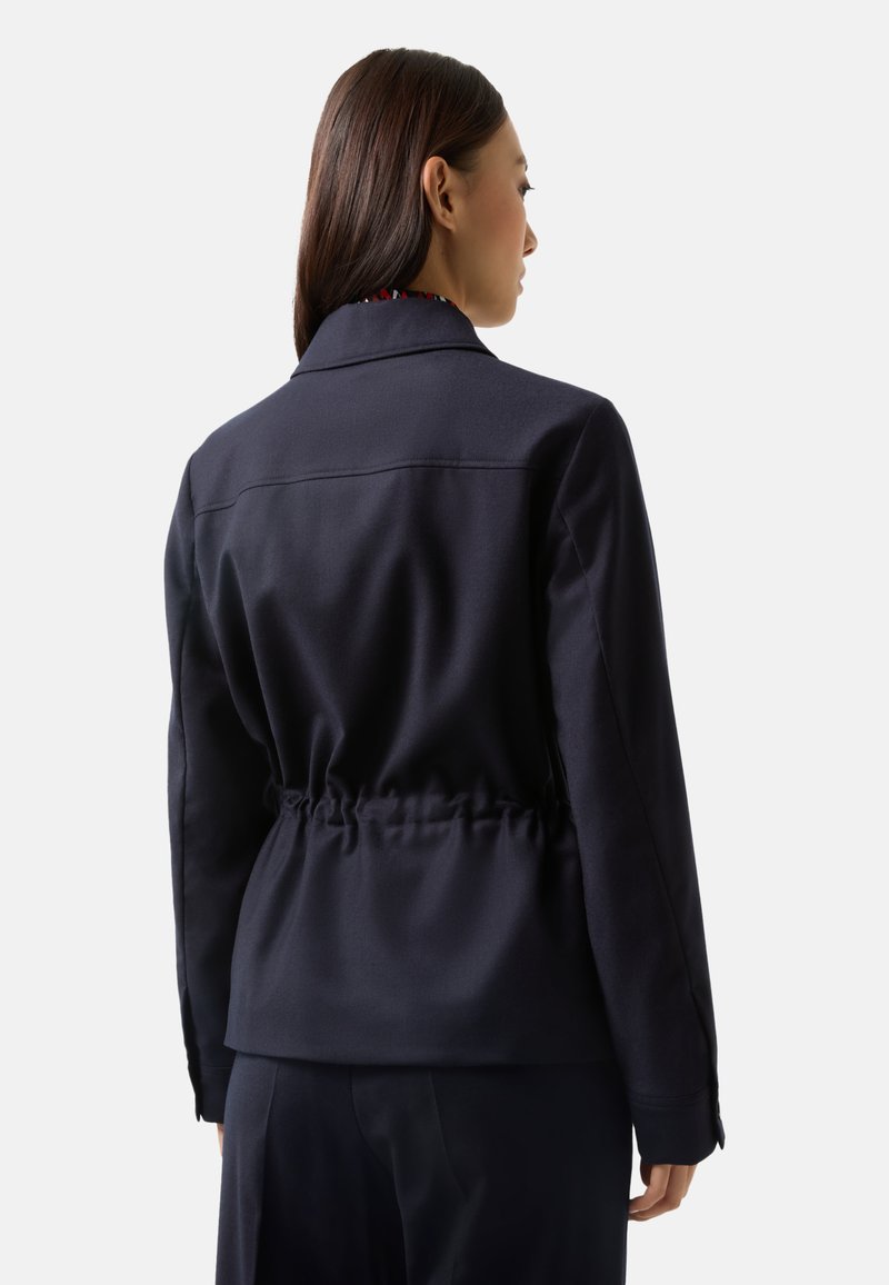 Marineblaues Jacket mit tailliertem Schnitt, strukturiertem Kragen und langen Ärmeln. Glatte Textur mit Schulternähten und einem subtilen Design.