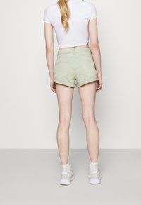 Vaaleanvihreät farkkushortsit, joissa on käänteet ja takataskut, yhdistettynä valkoiseen lyhythihaiseen t-paitaan ja valkoisiin urheilukenkiin.