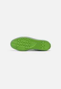 Suela de goma verde con patrones de agarre texturizados y marca. La parte superior es minimalista con un sutil tono gris.