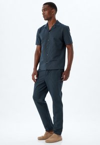 Kortärmad skjorta med knappar och matchande byxor i mörkblått med ett texturerat mönster. Mjuk tyg med en avslappnad passform och subtil glans.