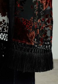 Fular negru semitransparent cu modele de catifea florale roșii și maronii, marginit cu un tiv ciufulit negru și detalii intricate de croșetat.