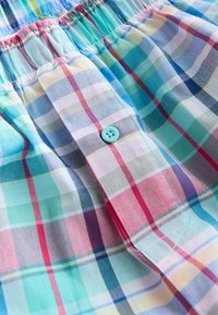 Gros plan sur un tissu à carreaux pastel avec des rayures roses, bleues et vertes, présentant un bouton bleu et un détail de ceinture élastique.