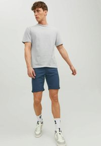 T-shirt a righe grigie e bianche, maniche corte, abbinato a pantaloni corti blu scuro con risvolti e sneakers bianche con dettagli grigi.