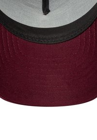 Cappello bordeaux con visiera nera; presenta un tessuto testurizzato, cuciture visibili e un interno grigio. Dettaglio con bottone al centro nella parte superiore.