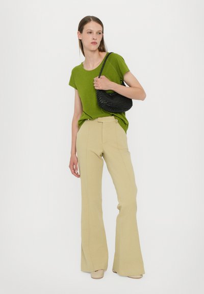 Green short-sleeve shirt, beige flared trousers, and black woven handbag; model displays a relaxed fit and simple design with minimal detailing.
