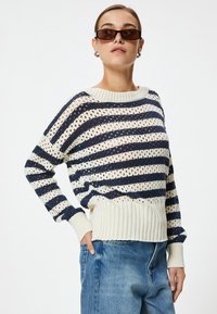 Gebreide trui met marineblauwe en crèmekleurige strepen, met opengewerkt patroon en geribde zoom. Gedragen met high-waisted jeans voor een casual look.