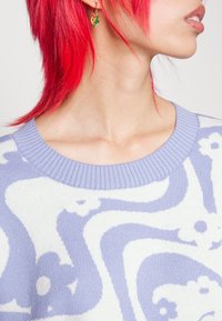 Knit sweater with a light lavender base, featuring white floral and wavy designs. Ribbed neckline and earrings in a green heart shape.