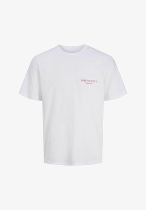 Garçon debout portant un t-shirt blanc à manches courtes, un jean bleu large et des chaussures beiges sur un fond blanc uni.